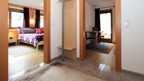 Camera d'albergo con un letto, un comodino e una scrivania con una sedia. Si apre una porta verso un'altra stanza.