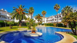 A swimming pool with a circular design, surrounded by palm trees and a white building with balconies. - San Esteban by Interhome (Jávea)