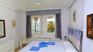 A bedroom with a bed, a chair, a radiator, and two windows with curtains. - San Esteban by Interhome (Jávea)