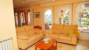 A living room with two beige sofas, a wooden coffee table, and a view through arched windows to the outside. - San Esteban by Interhome (Jávea)