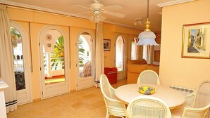 A dining area with a round table, wicker chairs, a ceiling fan, and a view through the glass doors. - San Esteban by Interhome (Jávea)