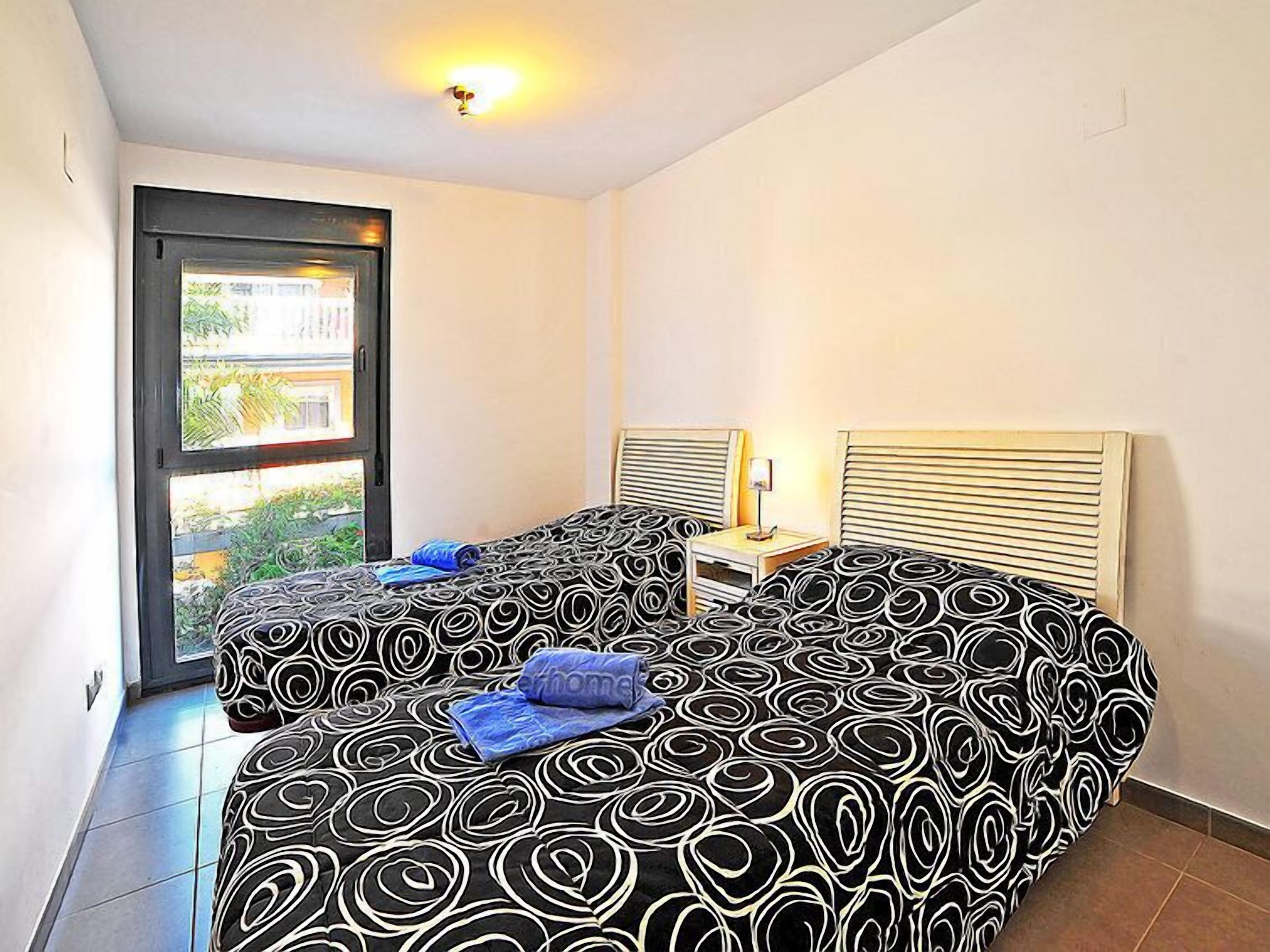 Une chambre d’hôtel avec deux lits, une fenêtre et une table de chevet avec une lampe.