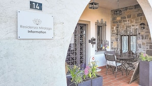 A building entrance with a sign reading 'Residencia Miralago Information,' a stone wall, an arched doorway, a wrought iron gate, and outdoor seating with plants. - Residenza Miralago Apt. C28 by Interhome (Piazzogna)