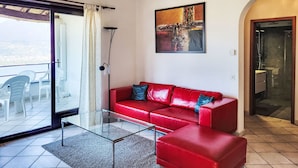 A modern living room with a red leather sofa, a glass coffee table, and a cityscape painting on the wall. - Residenza Miralago Apt. C28 by Interhome (Piazzogna)