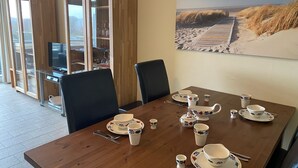 Ein Essbereich mit einem Holztisch, gedeckt für Tee, umgeben von Stühlen und einem großen Gemälde mit einer Strandansicht an der Wand.