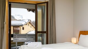 Een hotelkamer met een bed, een bankje voor de deur en uitzicht op met sneeuw bedekte bergen.