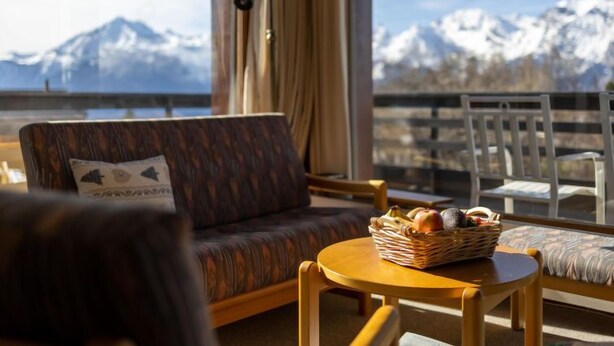 A cozy room with a sofa and chairs, a small table with a basket of fruit, and a view of snow-capped mountains. - Muverans I L2 by Interhome (Nendaz)