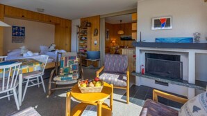 A cozy living room with a fireplace, a television, and a dining area with a table and chairs. - Muverans I L2 by Interhome (Nendaz)