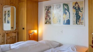 A hotel room with wooden paneling, a bed with white linens, a bedside lamp, and four abstract paintings on the wall. - Muverans I L2 by Interhome (Nendaz)