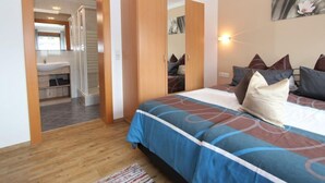 Un dormitorio con cama, almohadas, un espejo y un baño visible a través de una puerta abierta.