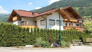 Un edificio de estilo chalet con techo inclinado, balcones de madera y un jardín bien cuidado con arbustos variados y un banco.