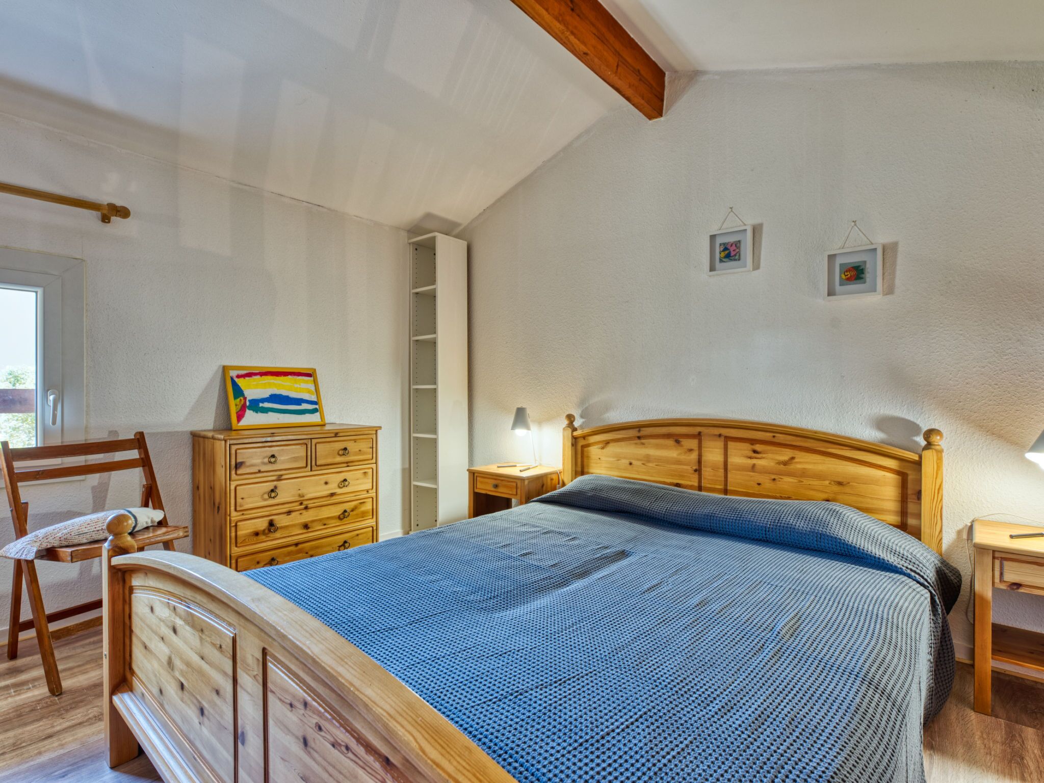 A bedroom with a wooden bed, a dresser, a chair, and a small bedside table with a lamp.
