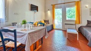A cozy room with a dining table, chairs, a bed, and a TV mounted on the wall. - Les Cracks - Les As by Interhome (Lacanau)