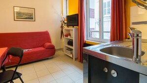 A compact kitchen with a sink, a red sofa, a television, and a window with curtains. - Bonsecours by Interhome (Deauville-Trouville)