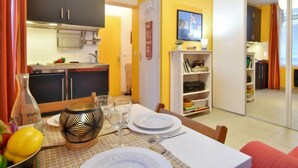 A dining area with a table set for four, a kitchen in the background, and a sliding door leading to another room. - Bonsecours by Interhome (Deauville-Trouville)
