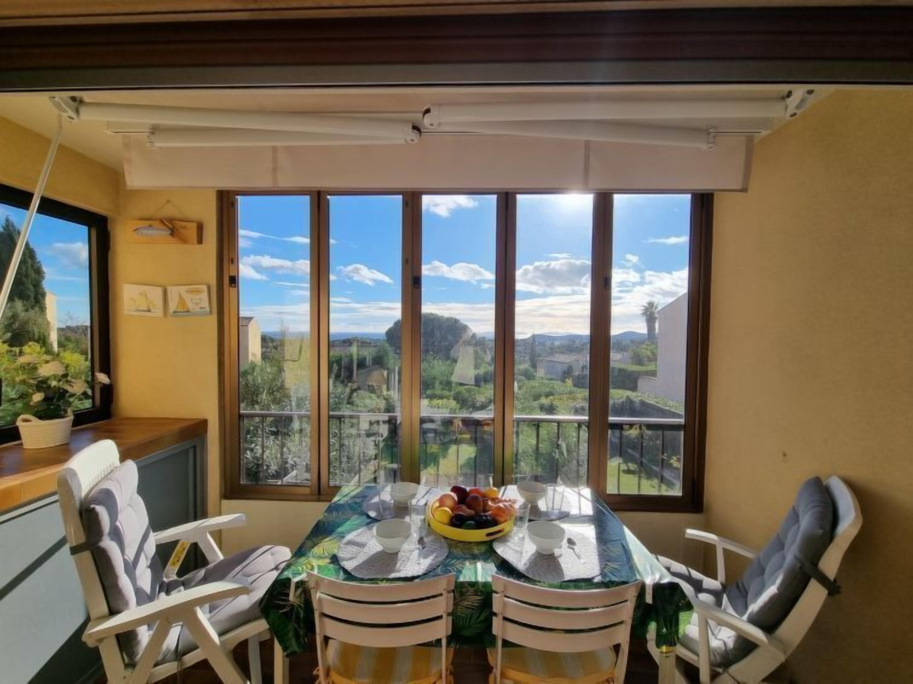 A dining area with a table set for four, large windows offering a view of a landscape with greenery and buildings.