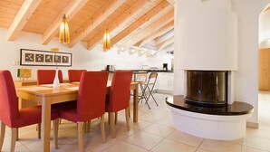 A modern interior with a wooden dining table, red chairs, a kitchen in the background, and a fireplace. - Apartment Aquila by Interhome (Zermatt)