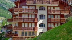 A multi-story hotel with wooden balconies, large windows, and a mountainous backdrop. - Apartment Aquila by Interhome (Zermatt)
