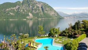 A resort with a swimming pool, lounge chairs, and a view of a lake with mountains in the background. - App. 511 by Interhome (Bissone)
