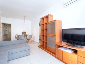A modern living room with a grey sofa, a wooden entertainment unit with a flat-screen TV, and a dining area with a table and chairs.