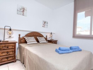 A bedroom with a wooden headboard, two bedside tables with lamps, a bed with beige bedding, two pillows with text, and a window with a view of buildings.