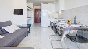 A compact living space with a sofa, a dining table with chairs, a kitchen area, and a TV mounted on the wall.