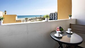 A balcony with a table set for two, overlooking a beach and a building.