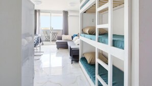 A modern, well-lit room with bunk beds, a sofa, a small table, and a view of the sea.