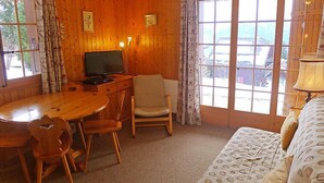 Um quarto acolhedor com paredes de madeira, uma mesa de jantar com cadeiras, uma televisão, um sofá e janelas amplas com cortinas.