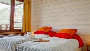 Un lit double avec deux oreillers, une fenêtre avec des rideaux jaunes et un mur en bois.