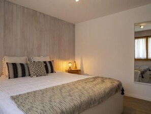 Quarto com cama, mesa de cabeceira, abajur e espelho na parede.