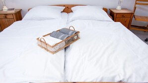 Ein ordentlich bezogenes Bett mit weißen Leinen, ein Korbwäscheschrank mit Handtüchern und Nachttische aus Holz mit Lampen.