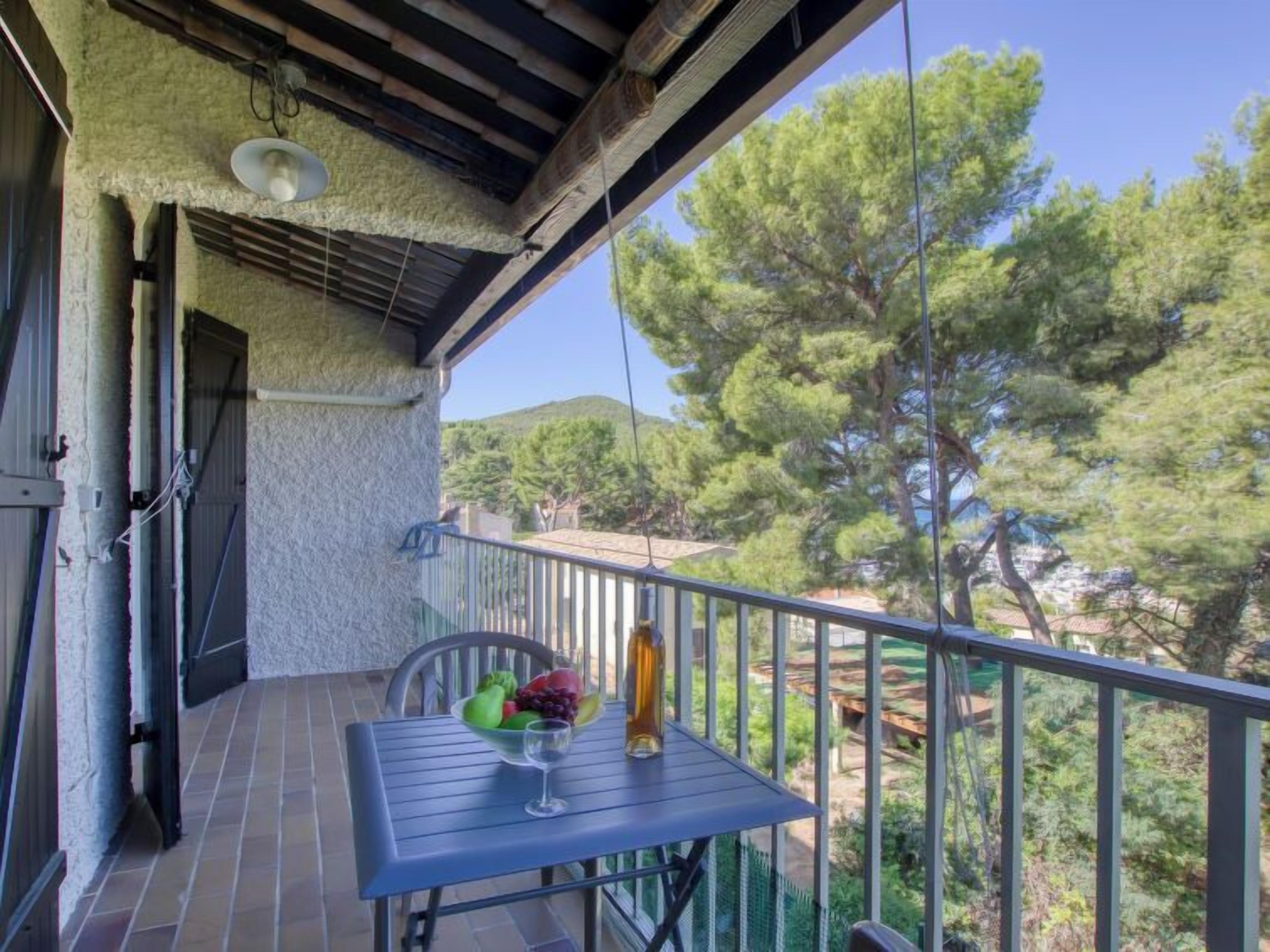 A balcony with a table set for two, a bowl of fruit, and a glass of wine.