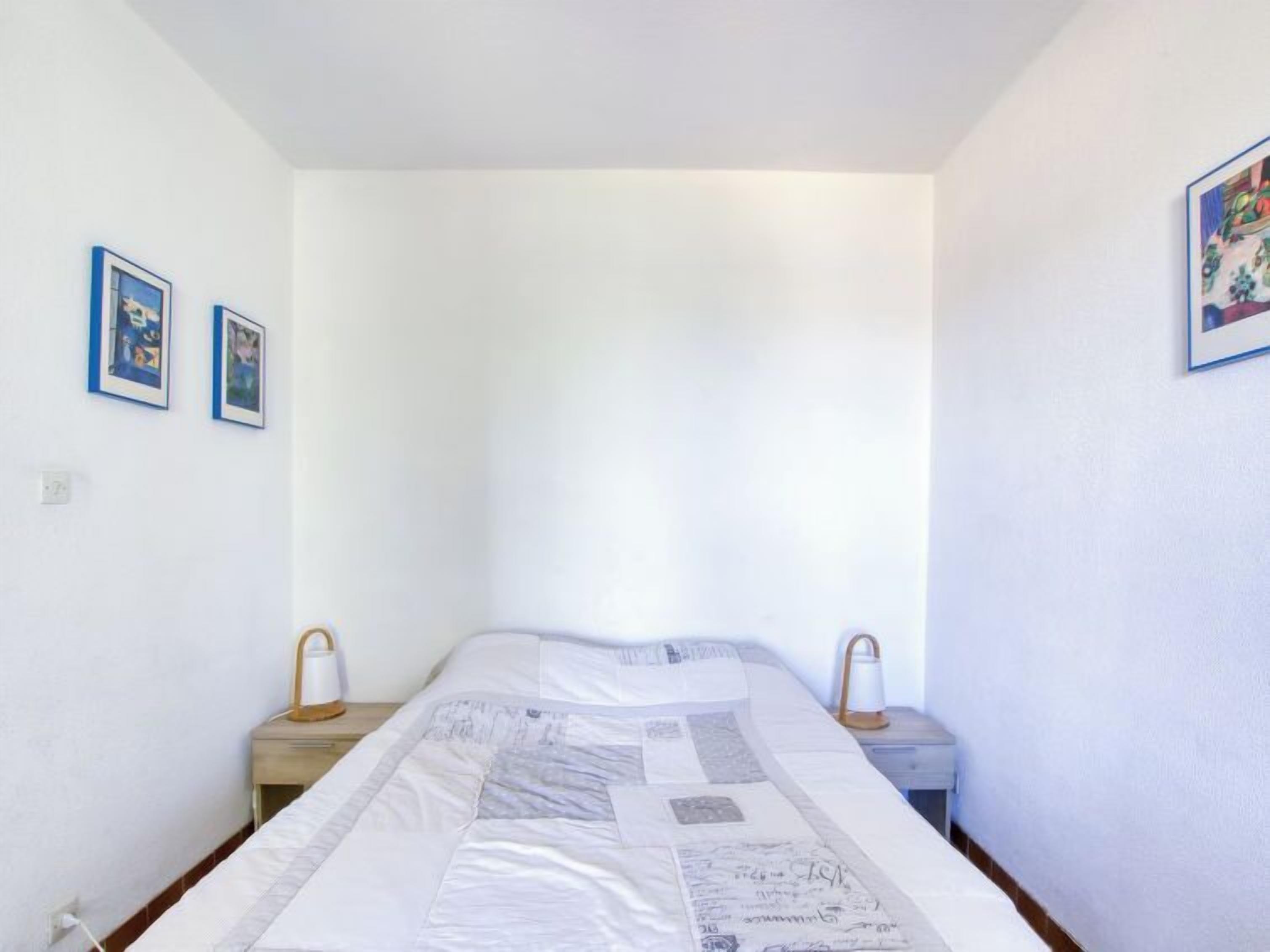 A small, simple room with a bed, two bedside tables, and two framed pictures on the walls.