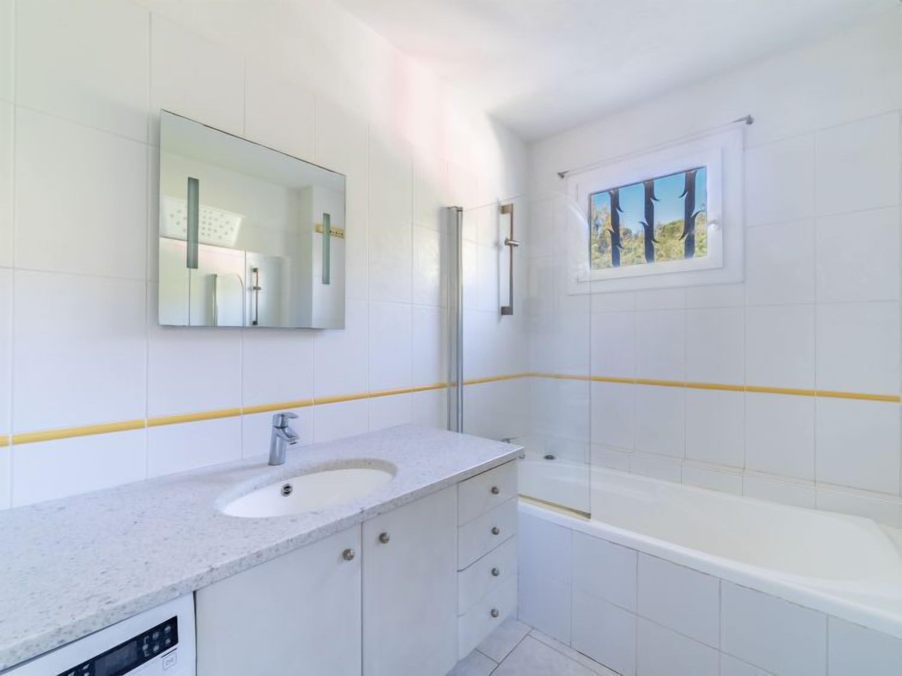Un baño moderno con lavamanos, espejo y bañera blancos.