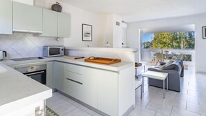 A modern kitchen with white cabinets, a microwave, and a dining area with a gray sofa and a table. - Carpe Diem by Interhome (Rayol Canadel)