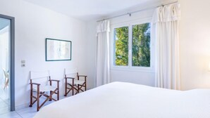 A bedroom with a large bed, two wooden chairs, a framed picture on the wall, and a window with curtains. - Carpe Diem by Interhome (Rayol Canadel)