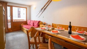 A dining area with a wooden table set for four, a sofa with a red blanket, and a window with curtains. - Le Hameau du Borsat (Val Claret) by Interhome (Tignes)