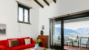Un salon moderne avec un canapé rouge, une table basse en bois et une vue sur les montagnes, visible à travers une grande porte-fenêtre coulissante.