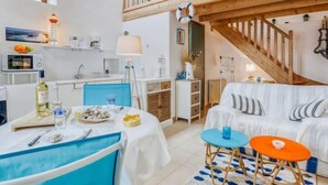 Una habitación acogedora con una mesa de comedor lista para dos personas, un sofá y una escalera que sube a un nivel superior.