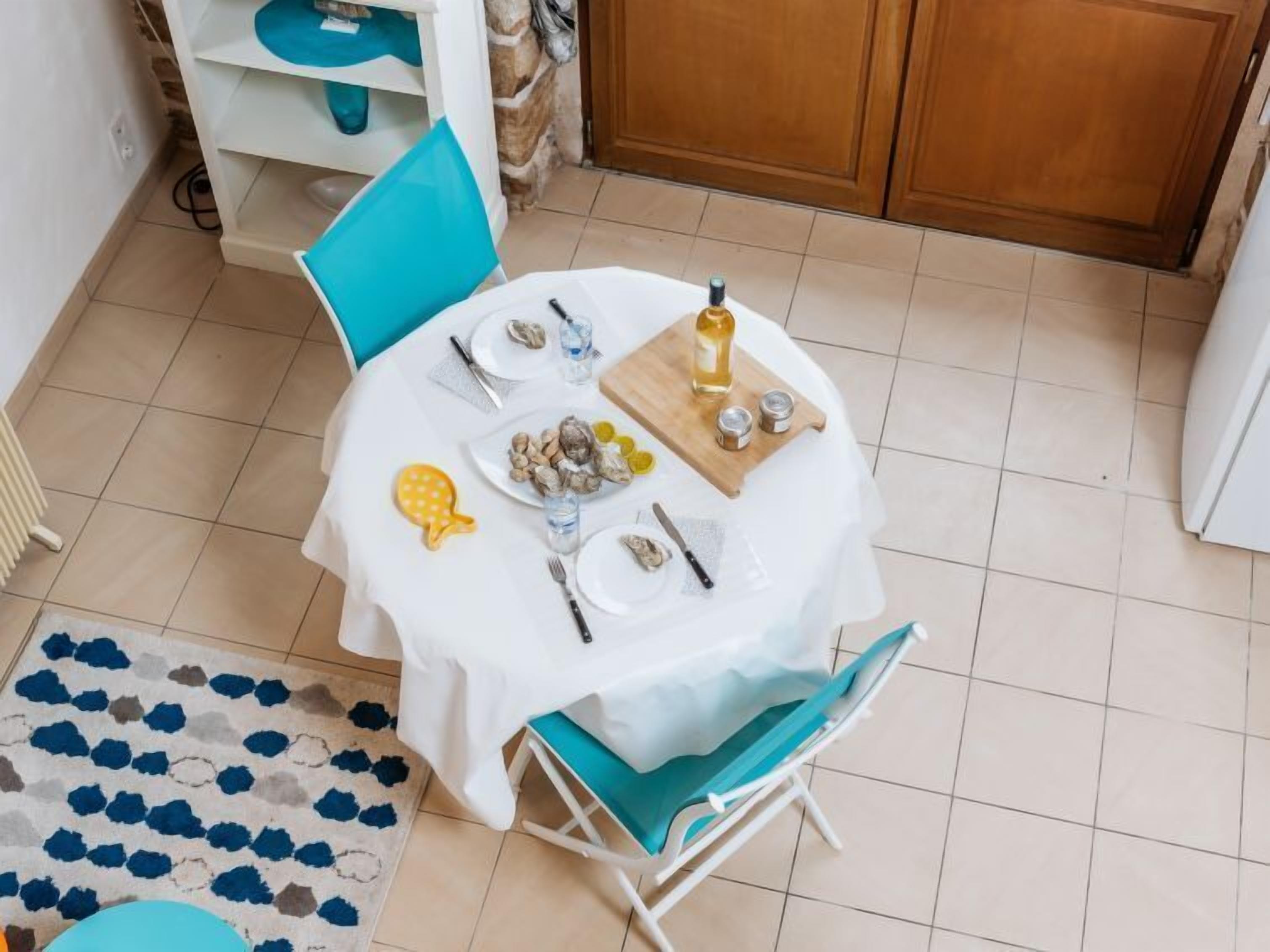 Une table à manger dressée avec des assiettes, des couverts et des condiments, entourée de chaises et surmontée d’un tapis à motifs.