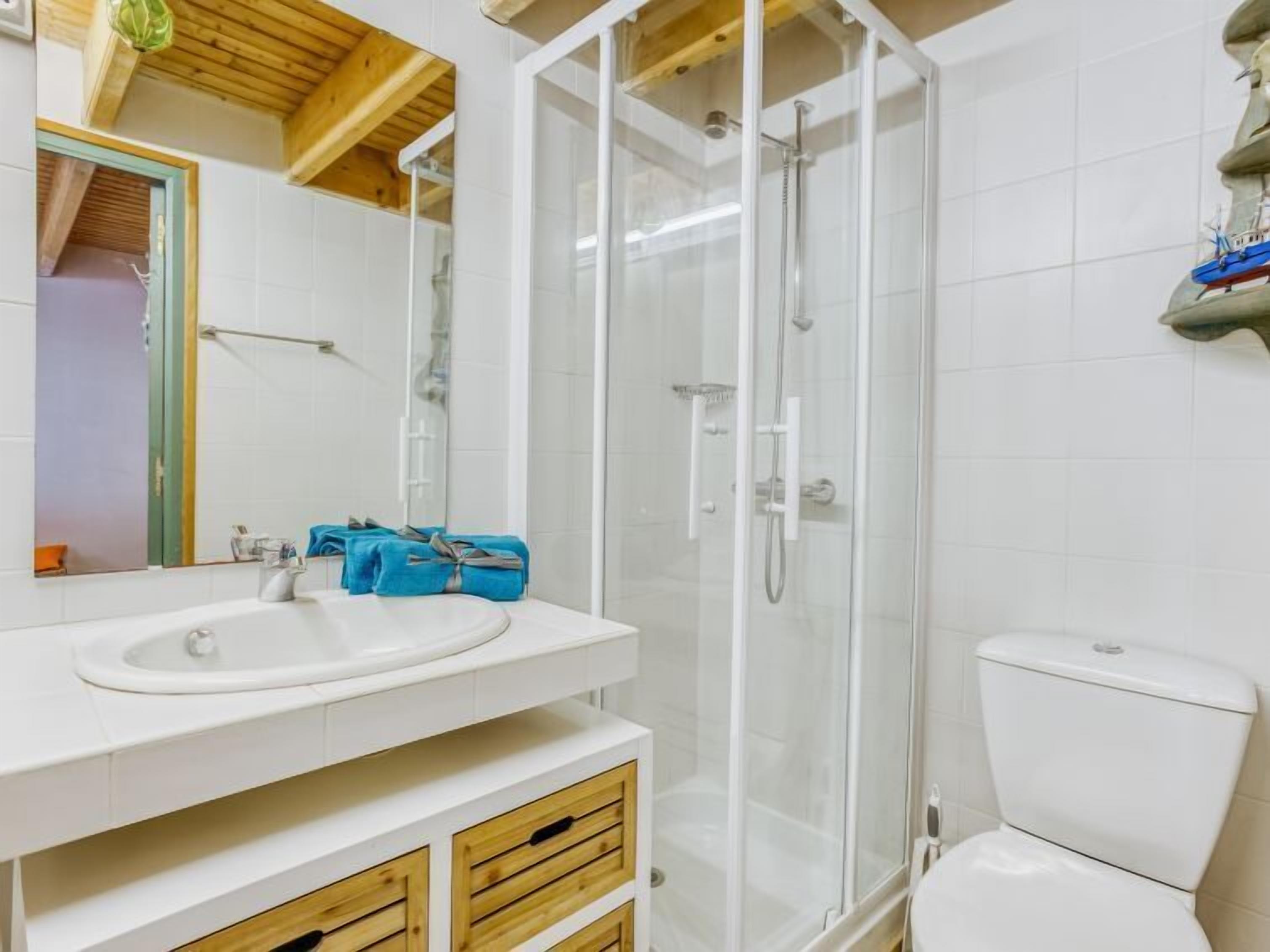 Uma casa de banho com uma pia branca, cabine de duche em vidro e sanita.