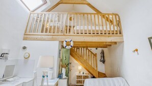 Un dormitorio tipo loft con una escalera de madera, un balcón pequeño y un tragaluz.