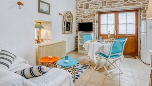 Un cuarto acogedor con pared de piedra, un televisor, una mesa de comedor con sillas, un sofá y una mesita de noche con lámpara.