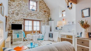 Una habitación acogedora con pared de piedra, televisión, mesa de comedor y zona de cocina.