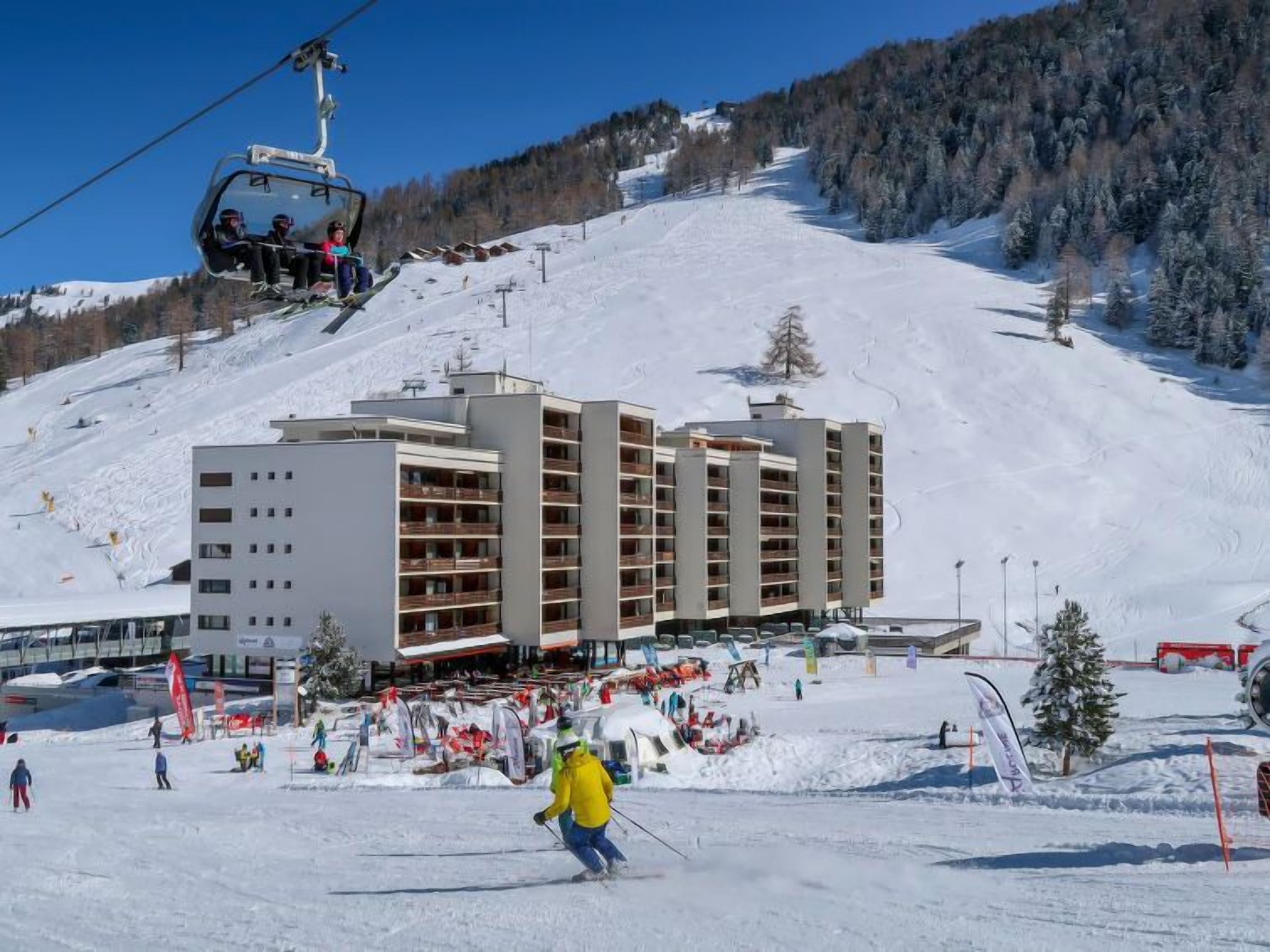 A ski resort with a multi-story hotel, ski lifts, and a snowy landscape.