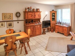 A cozy living room with a wooden dining table, chairs, a TV, and a cabinet with various items.
