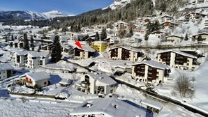 En snedækket bjerglandsby med bindingsværkshuse, en ski løjpe og en klar blå himmel.
