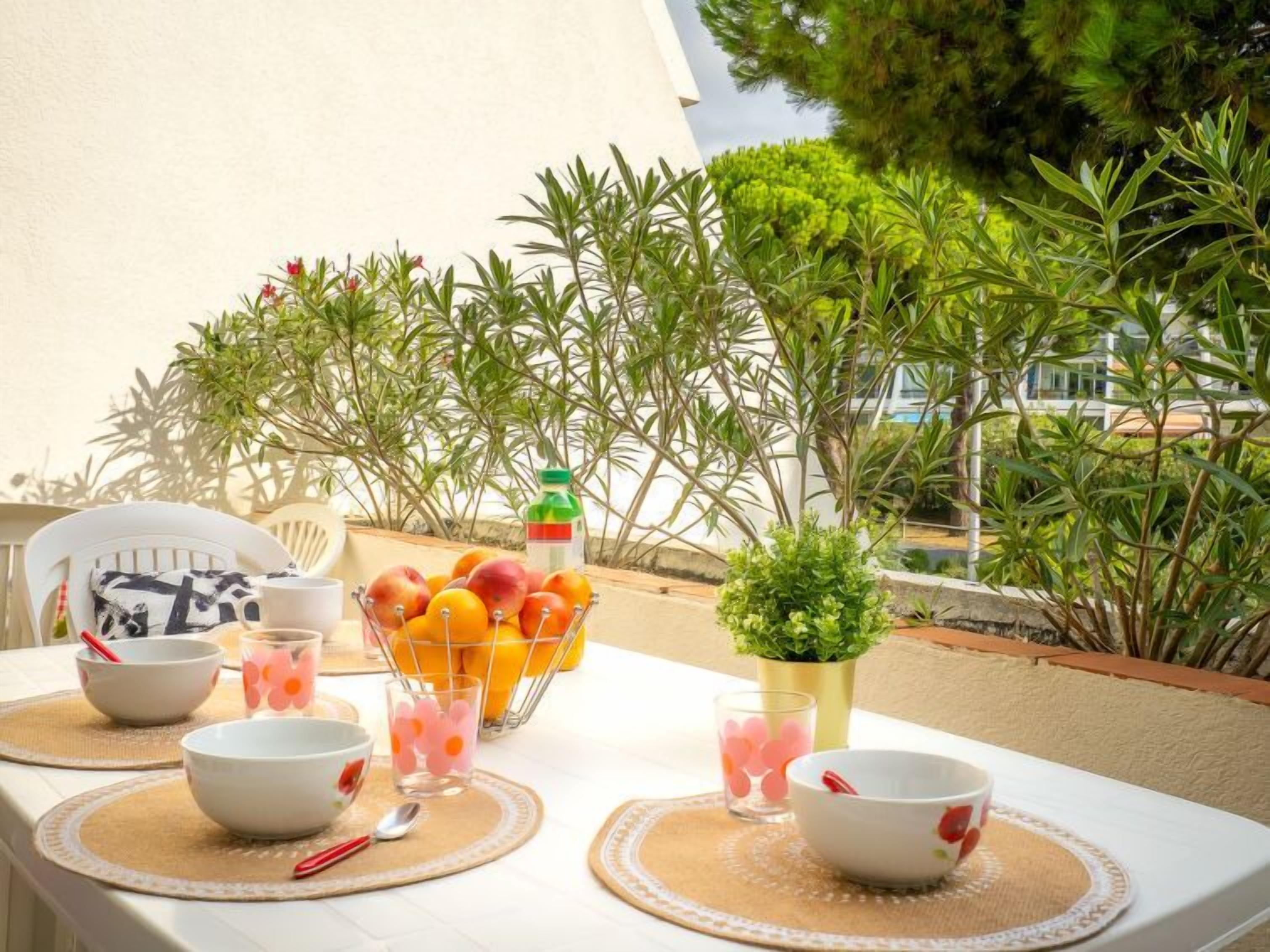 A table set outdoors with fruit, a juice bottle, and bowls.