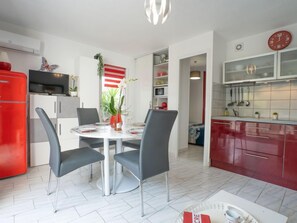 Eine moderne Küche mit roten Schränken, einem roten Kühlschrank und einem Essbereich mit einem runden Tisch und grauen Stühlen.